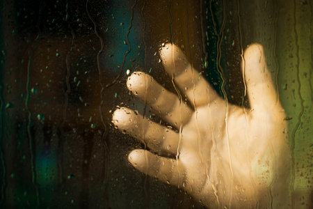 A man's hand in a window with rain drops. The concept of depression.