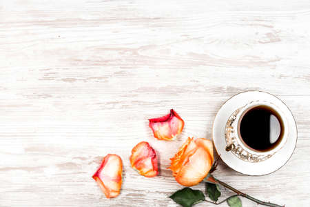 A cup of coffee, and an orange rose and petals on a background of vintage boardsの写真素材