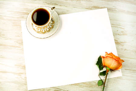 Bright red rose with a piece of paper with space for text, and a cup of coffee on a light backgroundの写真素材