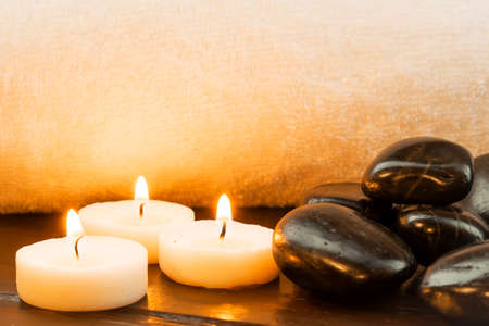 Dark stones and lit candles against a white towelの写真素材