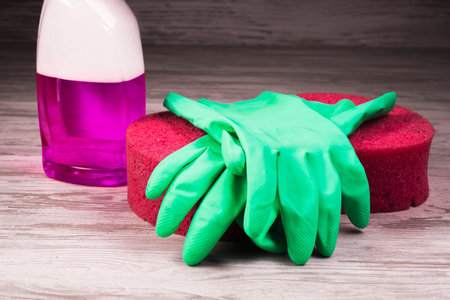 Items for cleaning, green gloves lying on a red sponge on a background of a spray with a violet...