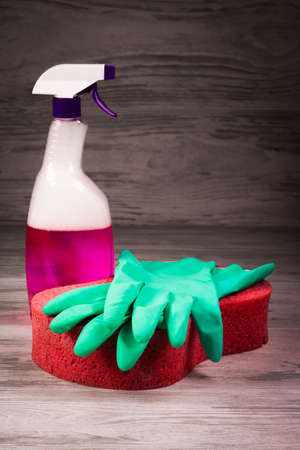 Items for cleaning, green gloves lying on a red sponge on a background of a spray with a violet liquidの写真素材
