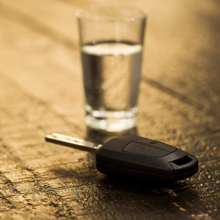The concept of driving under the influence of alcohol - car keys, a glass of alcohol on old boardsの写真素材