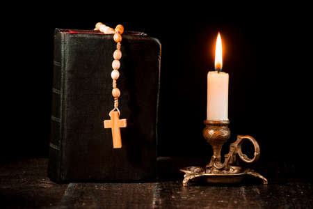 Rosary on the book, and a lit candle in a candlestick on a black backgroundの写真素材