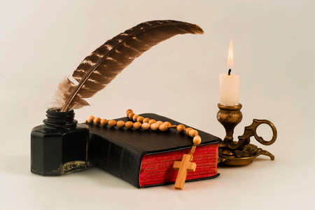 Book with a rosary and an inkwell with a pen, and a lit candle in the candlestickの写真素材