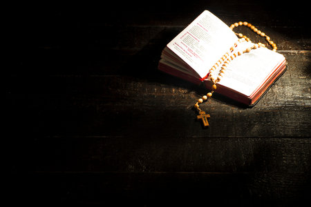 A bright book with a rosary on dark boards