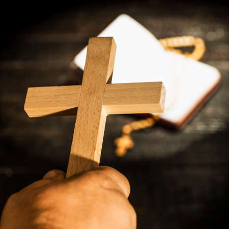 The cross held in the hand against the background of a lighted book with a rosaryの写真素材