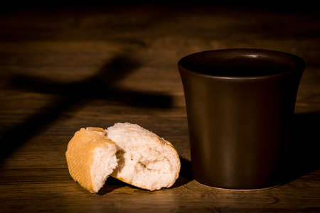 The concept of the multiplication of bread and wine in the Christian religion, bread and a brown cup of wine against the shadow of the crossの写真素材