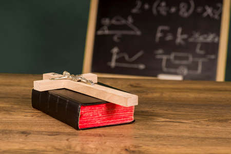 A crucifix on a book against the background of a written school boardの写真素材