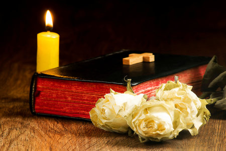 Old book, withered roses, a yellow candle and a cross on the book