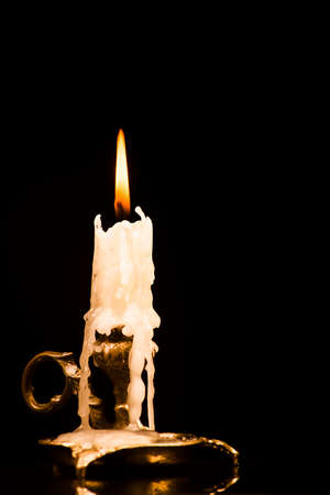Lit candle in a candlestick on a black background with molten waxの写真素材