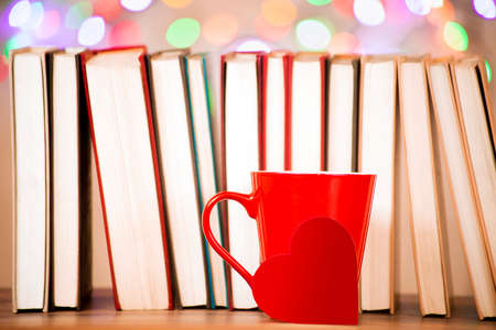 A red mug with a heart, against a background of a row of books and fuzzy lightsの写真素材