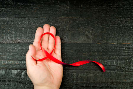 A red ribbon on the man's hand, against the background of the destroyed dark boardsの写真素材