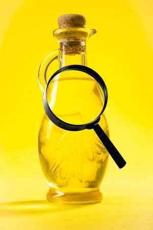 A magnifying glass on a background of oil bottles on a yellow backgroundの写真素材