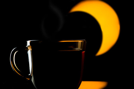 A cup with a hot drink with a yellow moon on a black backgroundの写真素材