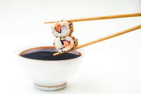 Sushi held in chopsticks over a bowl with sauce isolated on a white backgroundの写真素材
