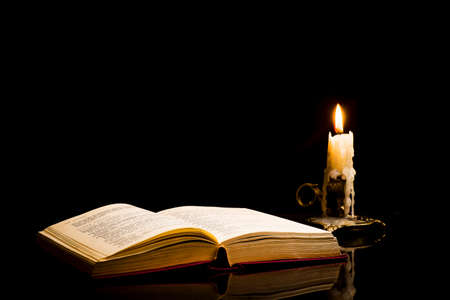 An open book with a lit candle on a black backgroundの写真素材