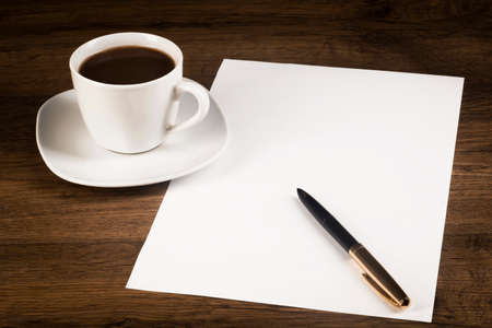 A cup of coffee, a white piece of paper with a pen on the desk topの写真素材