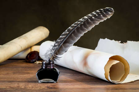 Feather with inkwell on the background of scrolls of papyrus on a brown countertopの写真素材