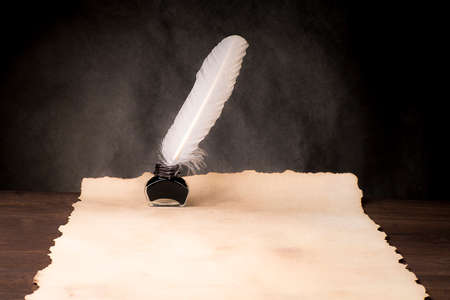 Unrolled scroll of papyrus with inkwell and bird feather on a countertop made of old boardsの写真素材