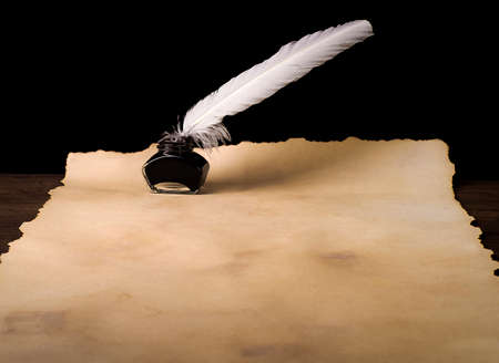 Unrolled scroll of papyrus with inkwell and bird feather on a countertop made of old boardsの写真素材