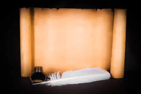 Unrolled scroll of parchment with a pen on a black backgroundの写真素材