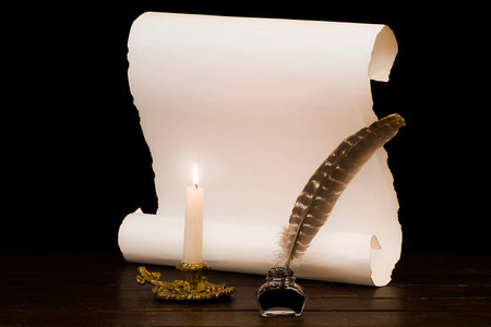 A lit candle and feather with inkwell against the background of an old scroll of parchment