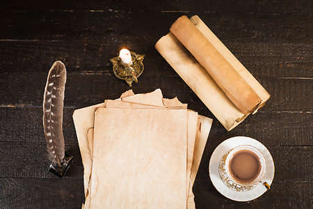A cup of drink, a scroll of papyrus, a feather, and a lit candleの写真素材