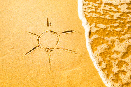 A drawing of the sun made on a yellow sandy beach inundated by a sea waveの写真素材