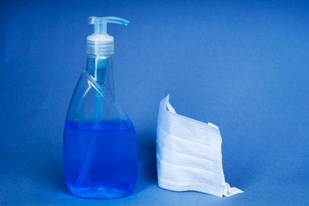 Virus protection concept - Sanitizing hand cleaner spray with cotton mask on blue backgroundの写真素材