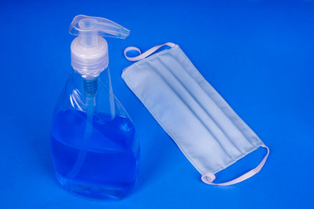 Virus protection concept - Sanitizing hand cleaner spray with cotton mask on blue backgroundの写真素材