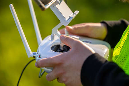 An unmanned aerial vehicle pilot in a reflective vest controls the drone using a flight controllerの写真素材