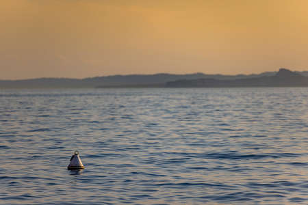 Italy - Lake Garda in the town of Torri del Benaco. Sunset, a buoy floating on the water, in the distance you can see the tops of the mountains.の写真素材