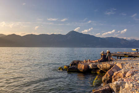 Italy - Lake Garda in the town of Torri del Benaco. A sunset, a romantic couple by the water, in the distance you can see the mountain peaks.の写真素材