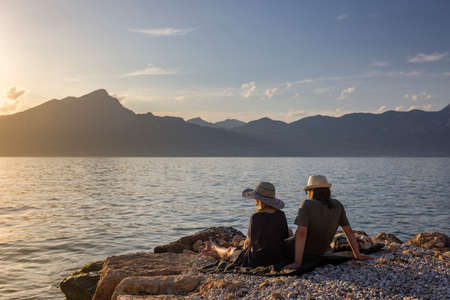 Italy - Lake Garda in the town of Torri del Benaco. A sunset, a romantic couple by the water, in the distance you can see the mountain peaks.の写真素材