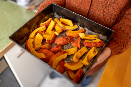 Honey-orange, baked hokkaido pumpkin in pieces with the skin on a baking tray held in your hands