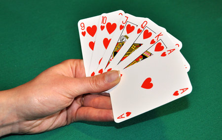 Hearts poker in womens hand, in front of green playing table