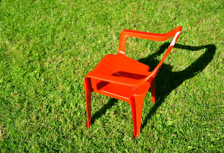 Empty red plastic chair on grass, droping shadowの写真素材