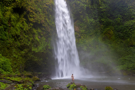 A young woman in a swimming suit at Nungnung waterfall in lush tropical forest, Bali, Indonesiaのeditorial素材