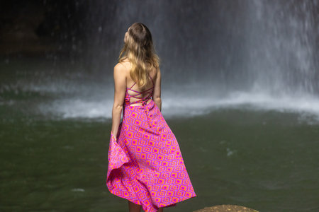 A young woman in a pink dress at Leke Leke waterfall in a lush tropical forest, Bali, Indonesiaのeditorial素材