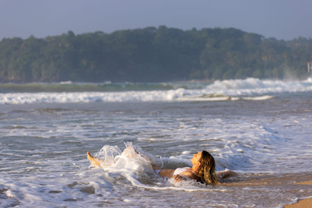 Young Woman Lying on the Shoreline as Waves Wash Over Her at Talalla Beach, Sri Lankaのeditorial素材
