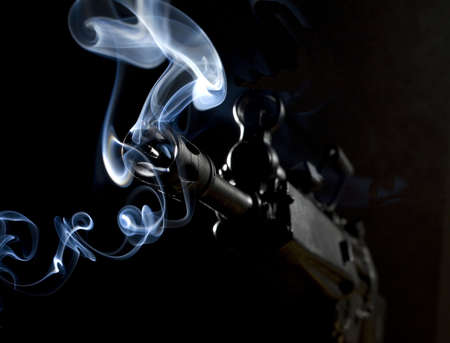 assault rifle that is smoking in the dark after a shotの写真素材