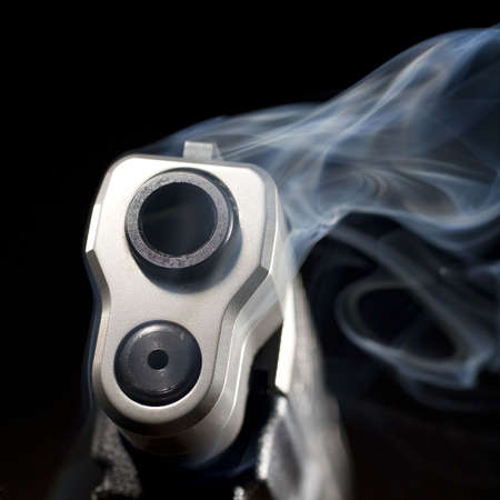 Blue smoke that is rising from the muzzle of a handgunの写真素材