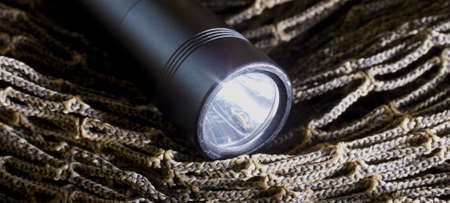 Black tactical flashlight that is on brown nettingの写真素材
