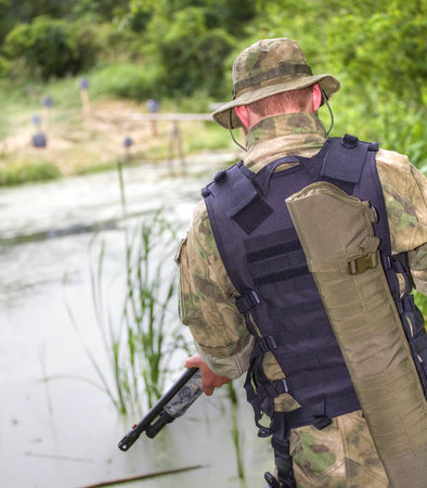 Man in camouflage with a shotgun keeping guard on a river
