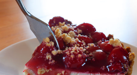 Fork going through cherrie frosting on a graham cracker crusted cheesecake