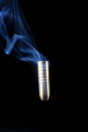 Copper bullet on a black background going down with smoke behindの写真素材