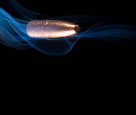 Copper plated bullet cruising in a cloud of smoke with a black backgroundの写真素材