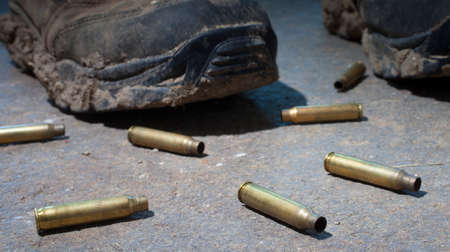 Boots with lots of mud with rifle cartridges on concreteの写真素材