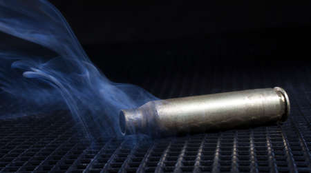 Rifle cartridge on a black grate with smoke aroundの写真素材